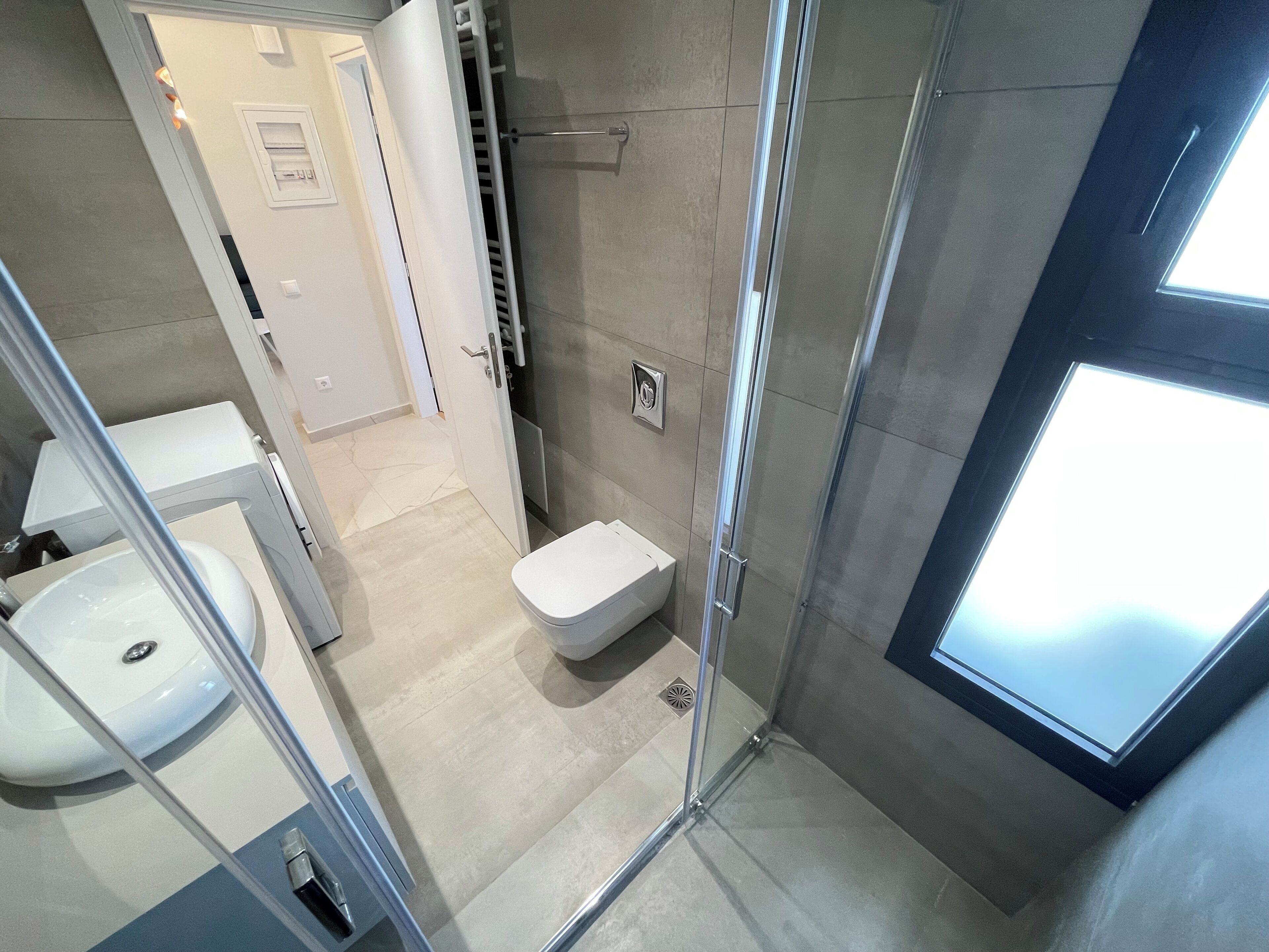 A modern bathroom with a glass-enclosed shower, a toilet, and a sink.