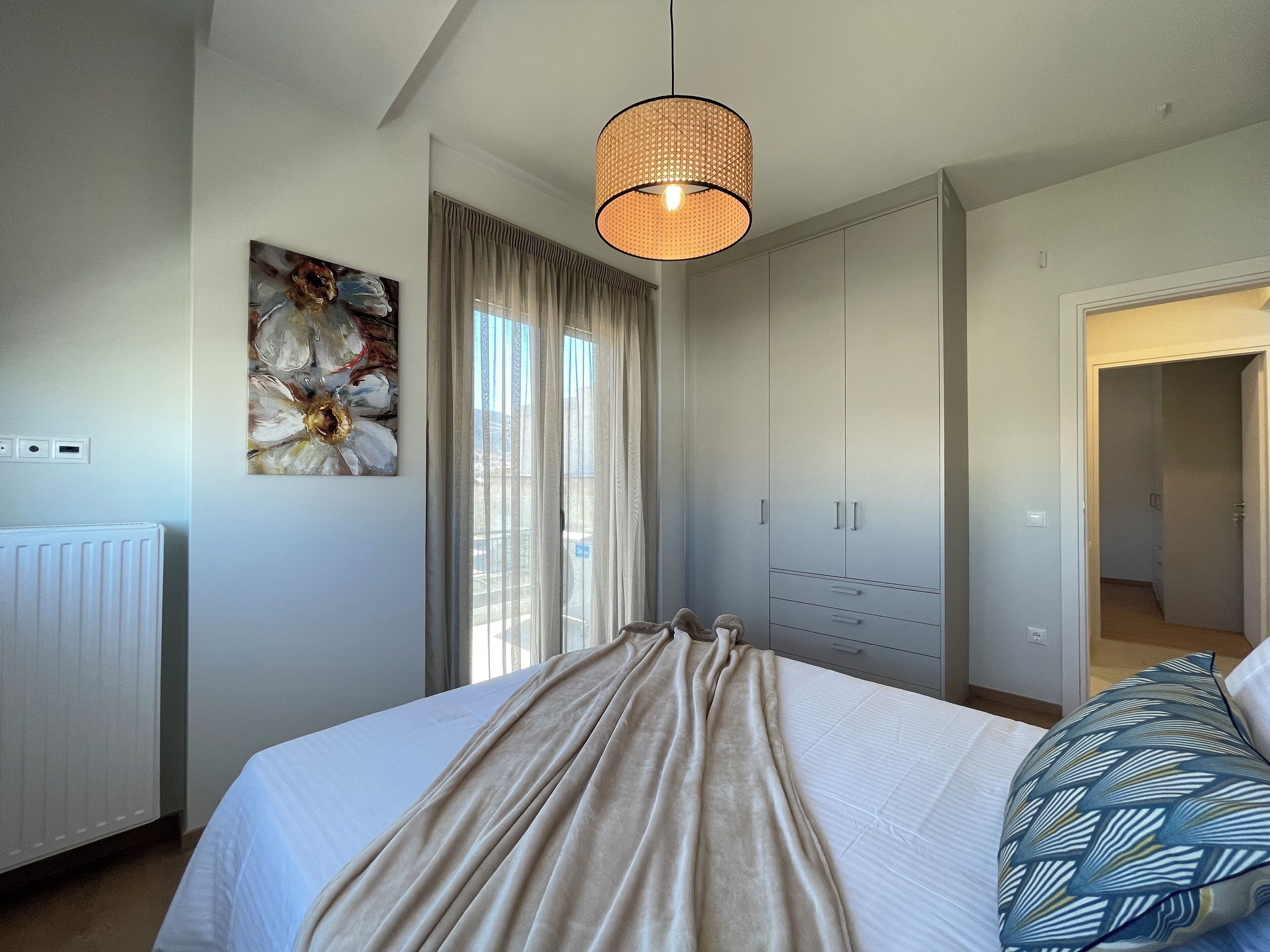 Quarto com cama, guarda-roupa grande, radiador, quadro e luminária pendente.