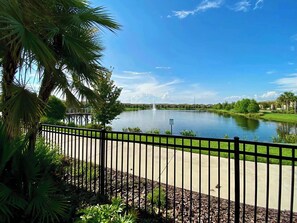 A serene lake with a fountain, surrounded by lush greenery and a clear blue sky.