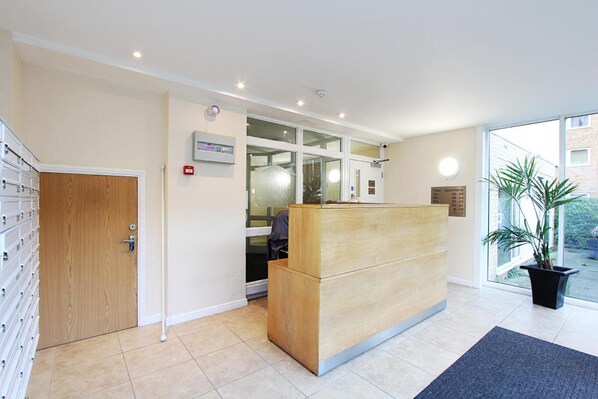 A reception area with a wooden reception desk, a glass door, a fire alarm, and a sign indicating apartment numbers.