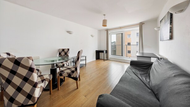 Ein modernes Wohnzimmer mit einem Glastisch, karierten Stühlen, einem grauen Sofa und Blick auf ein Gebäude durch ein großes Fenster.