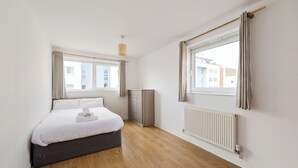 Ein Schlafzimmer mit Bett, Schrank, Heizkörper und einem Fenster mit Vorhängen.