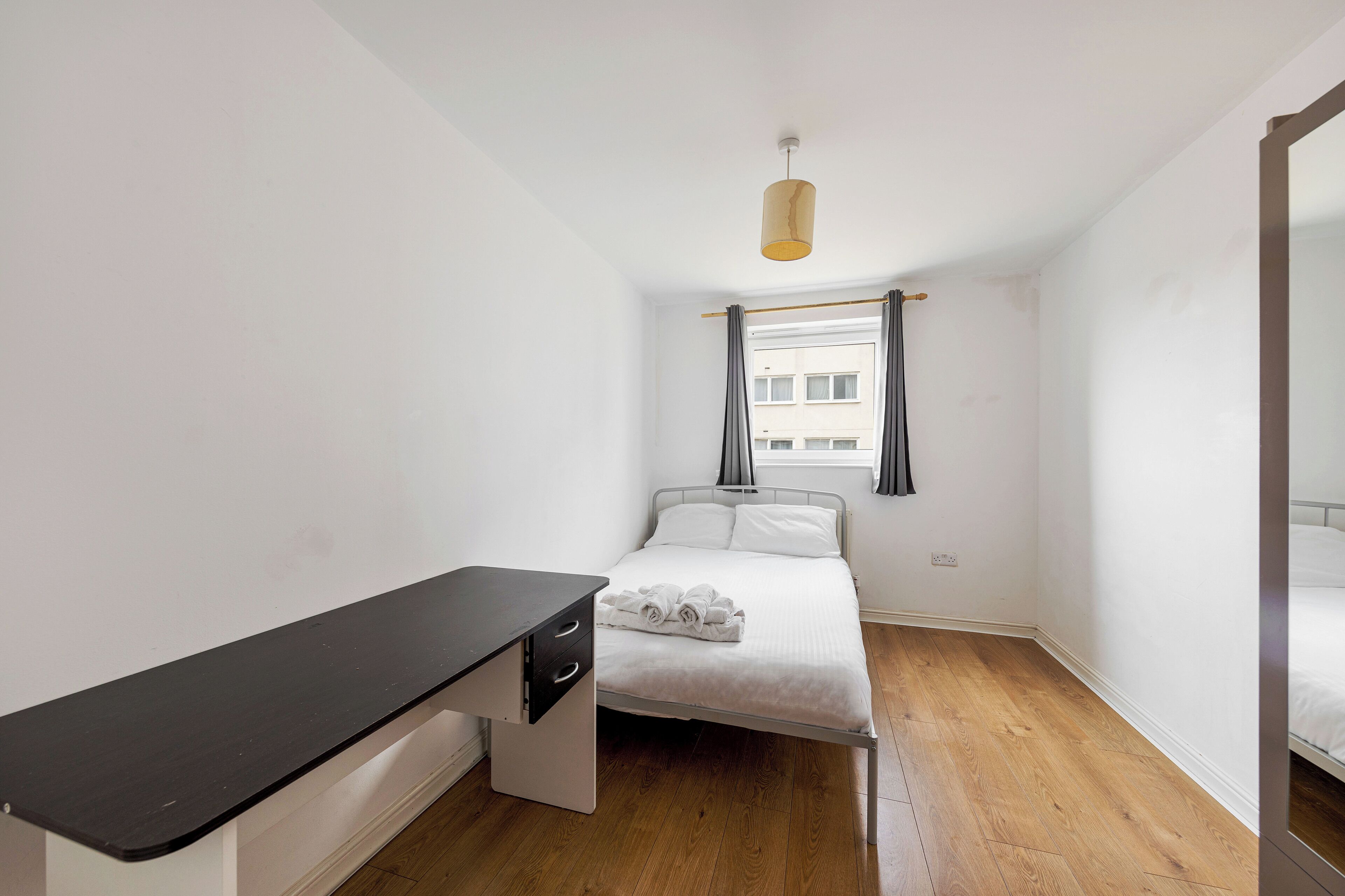 Ein kleiner, sauberer Raum mit Bett, Schreibtisch und einem fenster mit Vorhängen.