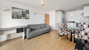Ein zeitgemäßer Wohnraum mit grauem Sofa, einem Glastisch mit karierten Stühlen, einer Küchenzeile und einem Stadtbild an der Wand.