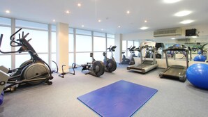 Ein Fitnessraum mit unterschiedlichen Trainingsgeräten, großen Fenstern und einer blauen Matte auf dem Boden.