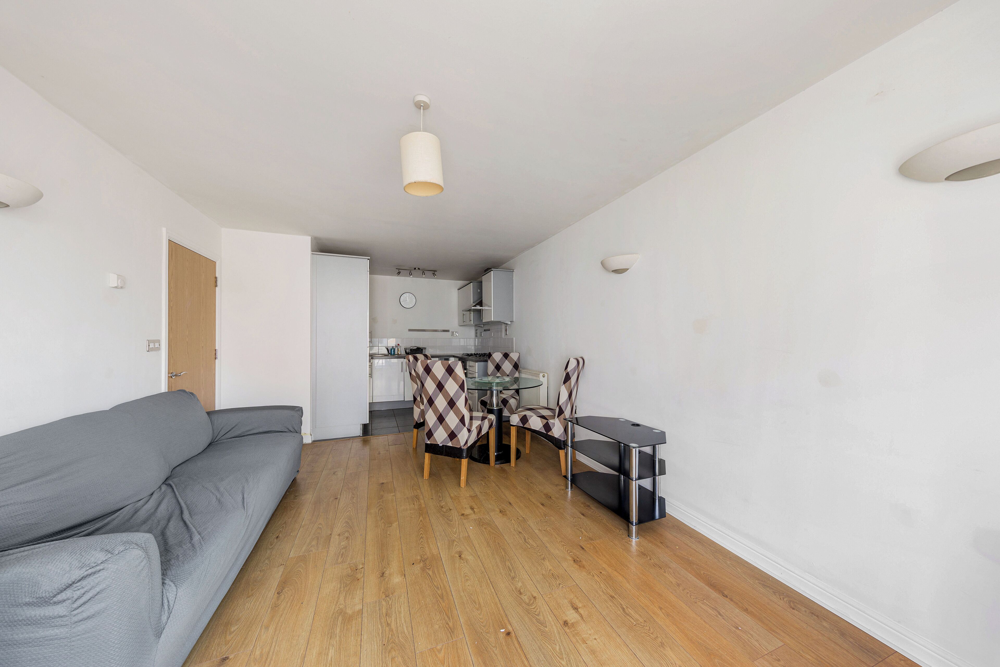 Een moderne woonkamer met een grijze bank, een eettafel met gestreept stoelen en een keuken op de achtergrond.