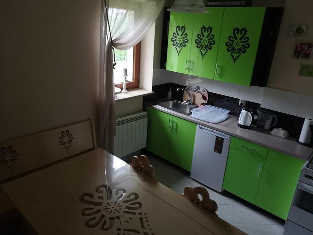 Une cuisine avec des meubles de couleur verte, un plan de travail blanc et une fenêtre avec un rideau.