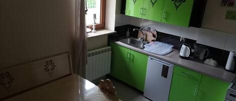 Une cuisine avec des meubles de couleur verte, un plan de travail blanc et une fenêtre avec un rideau.
