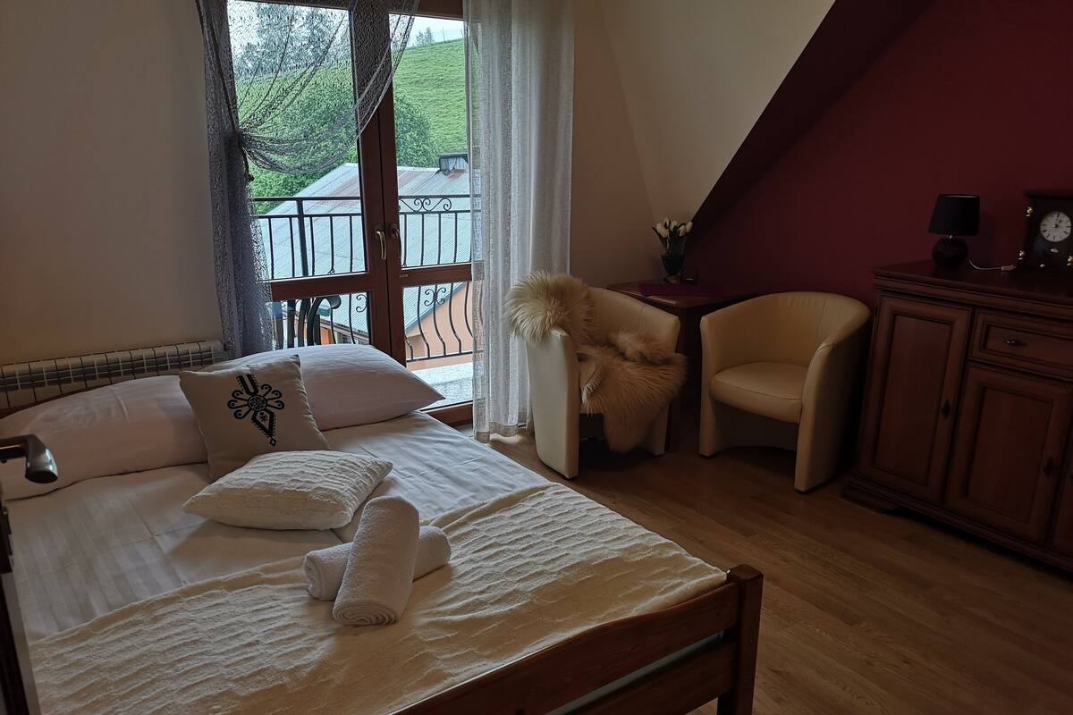 A bedroom with a bed, a chair, a nightstand, and a clock on a dresser.