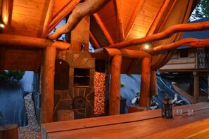 A rustic wooden structure with a stone fireplace, wooden beams, and a table with glasses and a lantern. - Pokoje Gościnne Pienińska Parzenica (Czorsztyn)