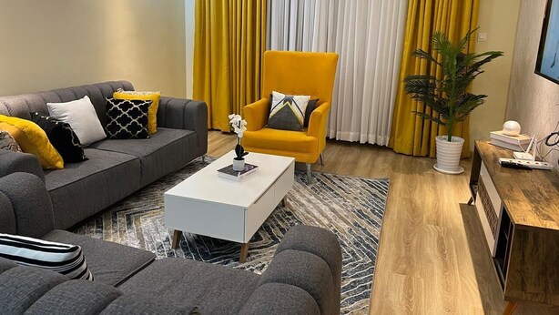 Een moderne woonkamer met een bank, fauteuil, salontafel en een potplant.