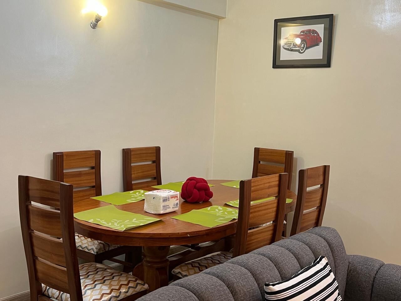 Un comedor con una mesa redonda de madera, seis sillas de madera, un objeto decorativo rojo y un cuadro en la pared.