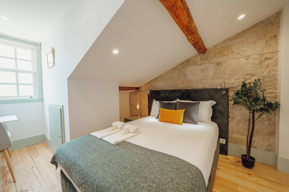 Une chambre avec un grand lit, une poutre en bois au plafond, un mur en pierre et une plante en pot.