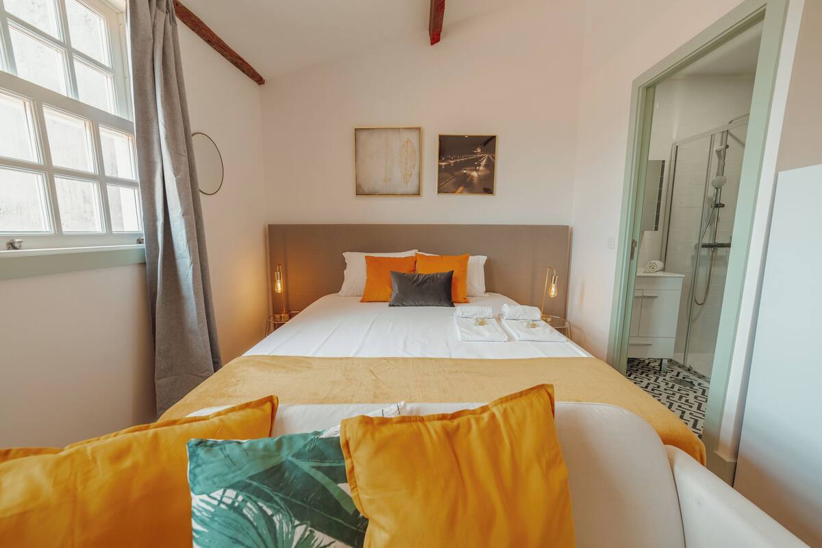 Un lit bien fait, avec une literie blanche et orange, une tête de lit et deux tableaux encadrés accrochés au mur.