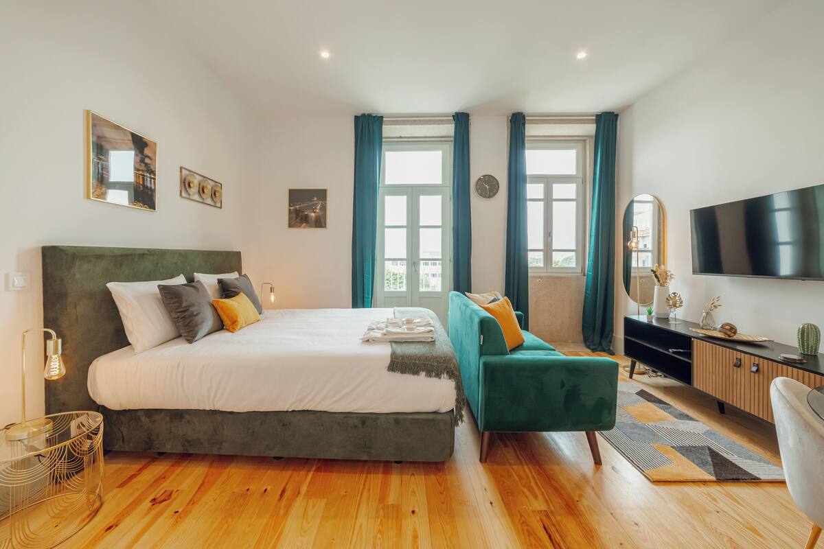 Une chambre moderne avec un grand lit, un fauteuil vert, une télévision et un plancher en bois.