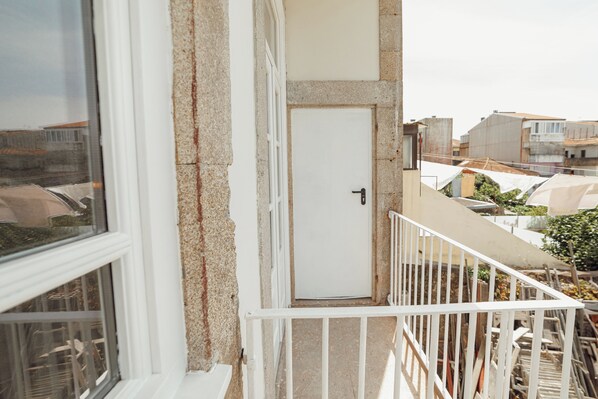 A balcony with a white door, a window, and a view of neighboring buildings.