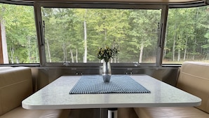 A table with a vase of flowers, cushioned seating, and a window with a forest view.