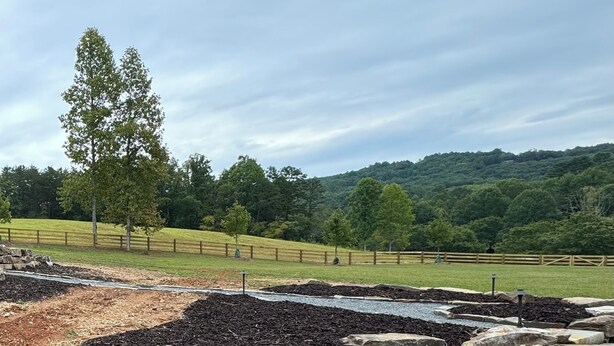 A rural landscape with a fenced area, trees, and a hill in the background.