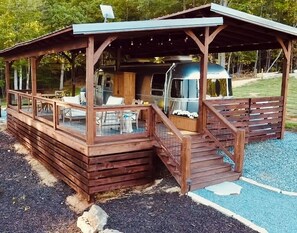Eine Holzhütte mit überdachter Terrasse, einem Grill und einem Wohnmobil darin.