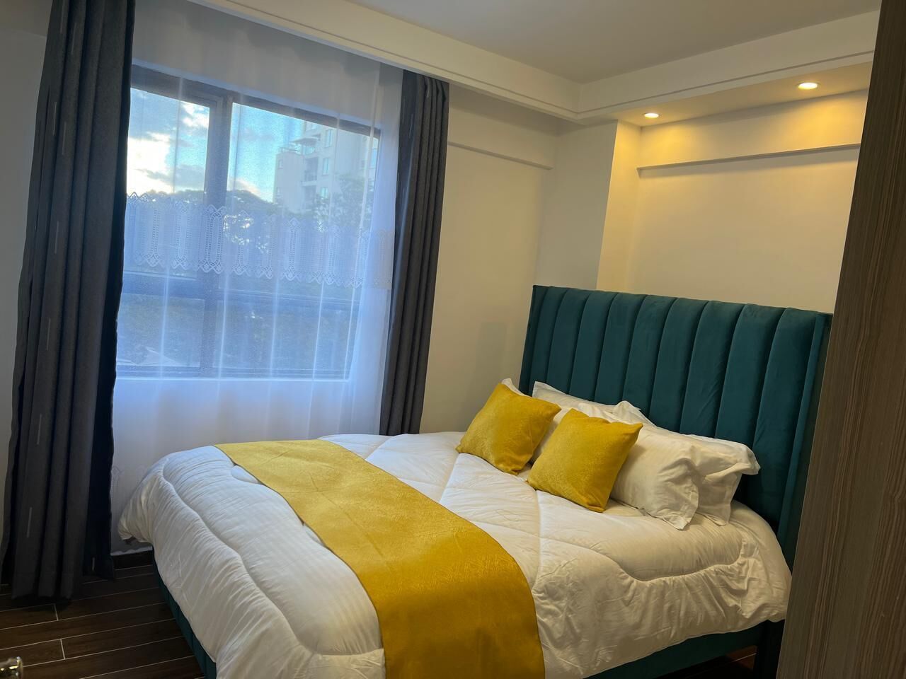 A hotel room with a bed, curtains, and a view of buildings outside.