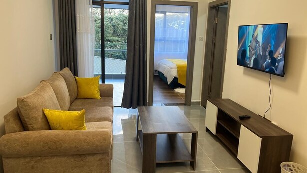 A modern living room with a sofa, coffee table, TV, and a balcony with a bed. - Valley Heights Apartments by Bliss Haven (Nairobi)