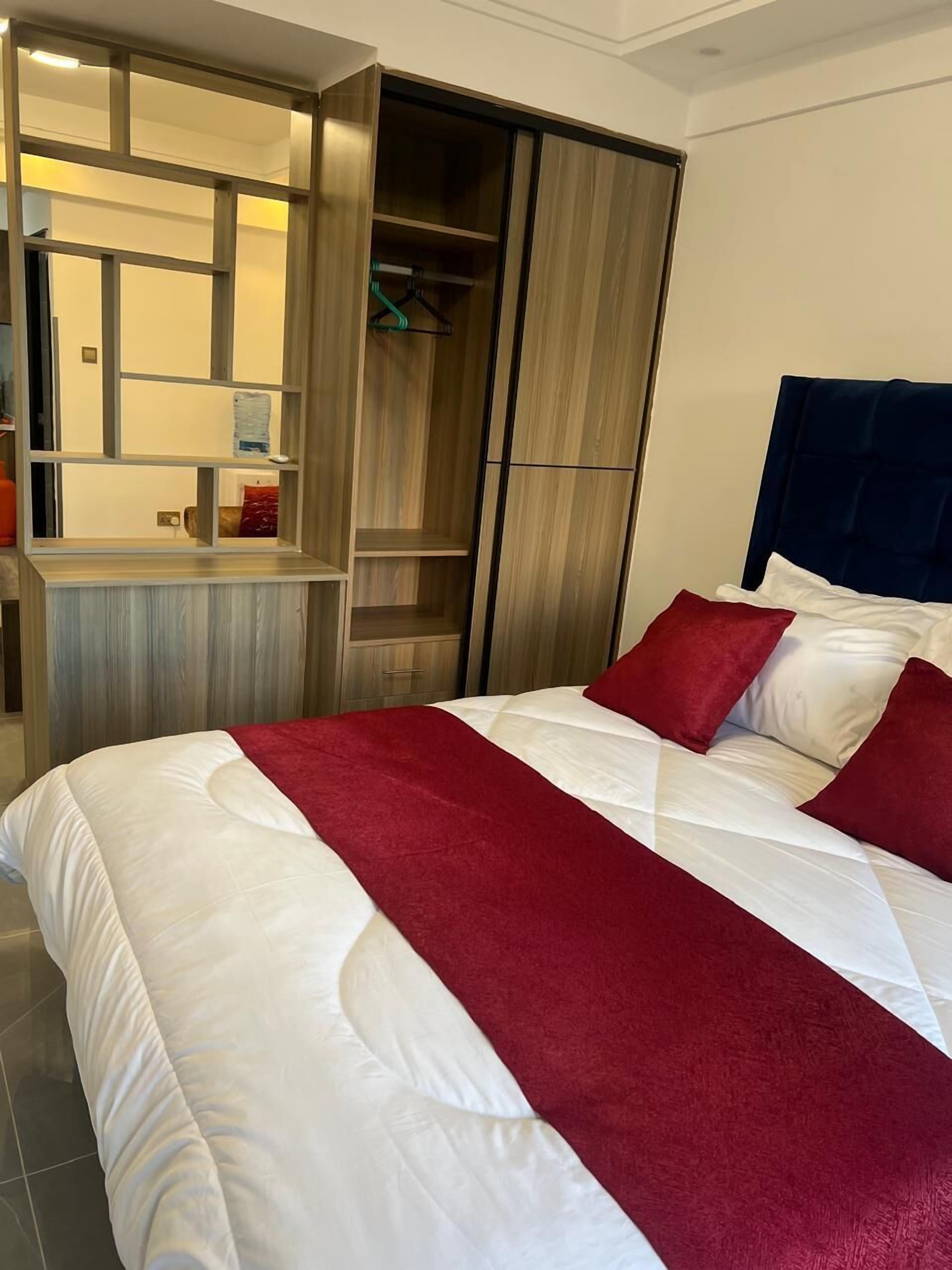 Una cama bien hecha con ropa de cama blanca y roja, un armario de madera con espejo y una pequeña zona de escritorio.