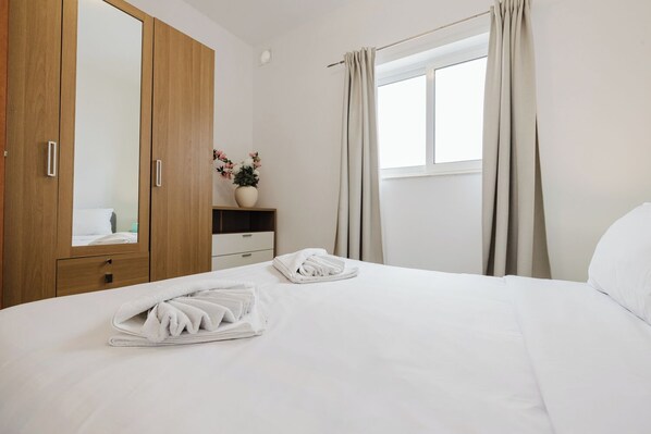 A hotel room with a bed, a wardrobe, a bedside table with a vase of flowers, and a window with curtains.