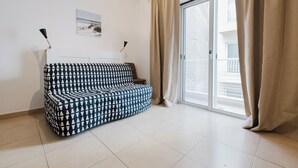 A modern living room with a patterned sofa, a small table, and a sliding glass door leading to a balcony. - Bright, comfortable 1-bedroom apartment in the heart of Sliema. Steps from the beach, promenade, shops, restaurants, and bus stops. Fully equipped with kitchen, Wi-Fi, air conditioning, and sofa bed. (Tas-Sliema)