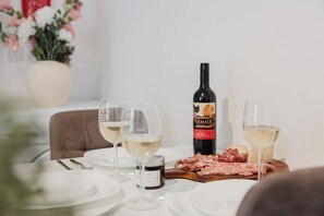 A dining table with white plates, two wine glasses, a bottle of wine, and a wooden board with sliced meats.