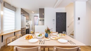 Un espace de repas moderne avec une table en bois dressée pour le repas, un vase rempli de fleurs et, en arrière-plan, une vue sur la cuisine.