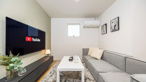 Un salon moderne avec un téléviseur à écran plat fixé au mur, un canapé gris, une table basse blanche et une petite fenêtre.