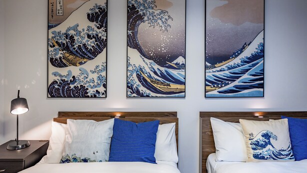 Une chambre d’hôtel avec deux lits, une table de chevet et trois œuvres d’art encadrées représentant des vagues.