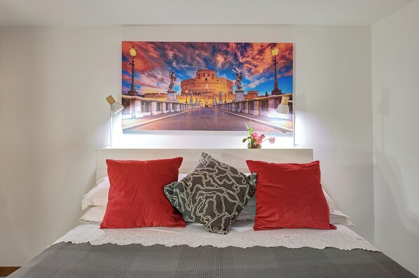 Un lit recouvert d’une housse de dentelle blanche, avec des oreillers rouges et un coussin à motifs.