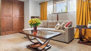 Un salon comprenant un canapé, une table basse avec un plateau en verre, une armoire en bois et une fenêtre ornée de rideaux jaunes.