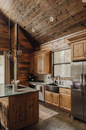A kitchen with wooden cabinets, a stainless steel refrigerator, and a hanging light fixture.