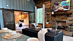 Acogedor interior de cabaña con sala de estar, chimenea y televisor mostrando un paisaje.
