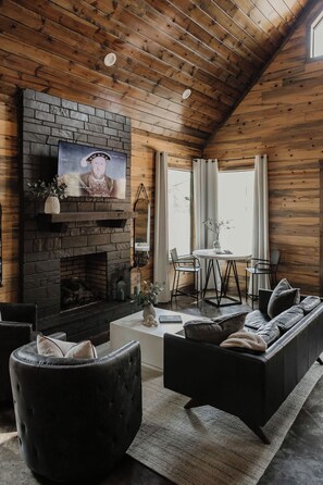 A cozy living room with a fireplace, a television mounted on a brick wall, and a comfortable seating area with a sofa and armchairs.