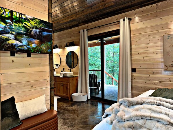 L’intérieur d’un chalet en bois comprend une salle de bain, un lit et un balcon offrant une vue sur la forêt.