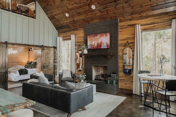 A spacious living room with a fireplace, a television mounted above it, and a dining area with a table and chairs.