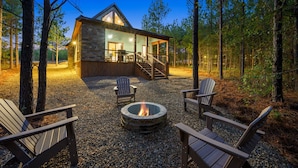 Una cabaña con fachada de piedra, una terraza y un pozo de fuego rodeado de sillas Adirondack.