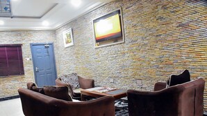 A room with a stone wall, a blue door, brown leather sofas, and a table with magazines. - Yewa Frontier Hotel (Ibese)
