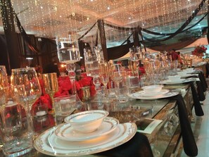 Una sala da banchetti con tavoli apparecchiati per un evento formale, con calici trasparenti e decorazioni raffinate.