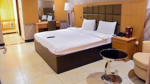A hotel room with a large bed, bedside tables, a desk, a chair, and a small round table. - Yewa Frontier Hotel (Ibese)
