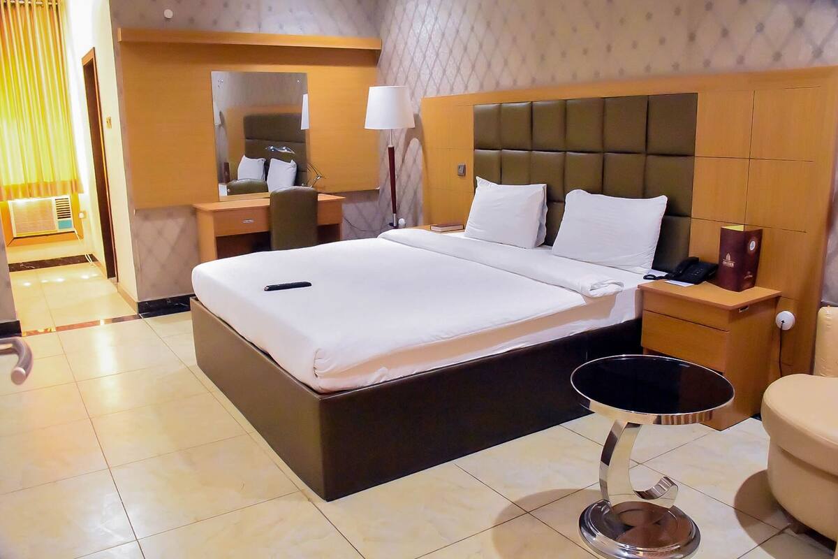 Ein Hotelzimmer mit einem großen Bett, Nachttischen, einem Schreibtisch, einem Sessel und einem kleinen runden Tisch.
