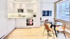 A modern kitchen with white cabinets, a microwave, oven, and a dining area with a glass table and chairs. - Bright 1Bed Flat Covent Garden (Greater London)