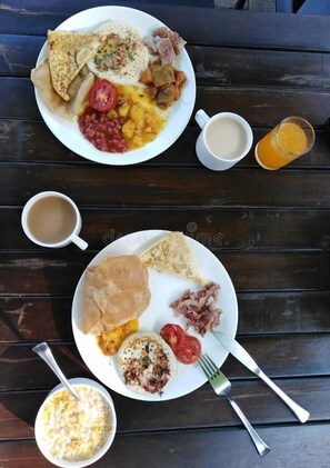 Two plates of food on a wooden table with a cup of coffee and a glass of orange juice.