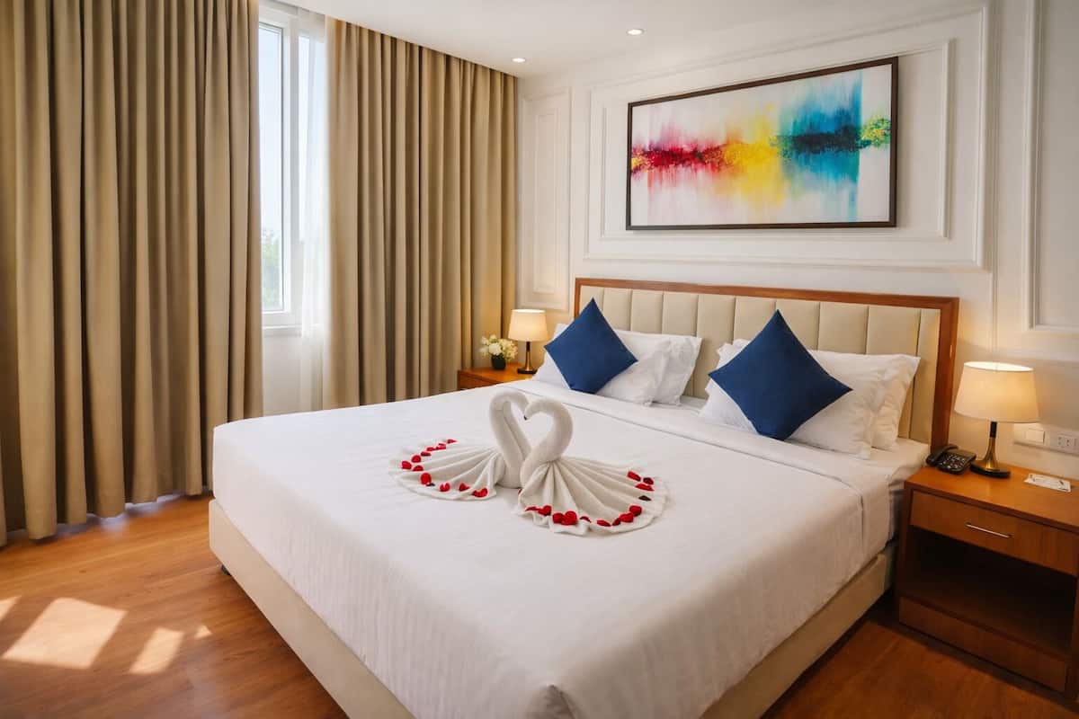 Habitación de hotel con una cama grande, dos almohadas, una mesita de noche, una lámpara y un cuadro en la pared.