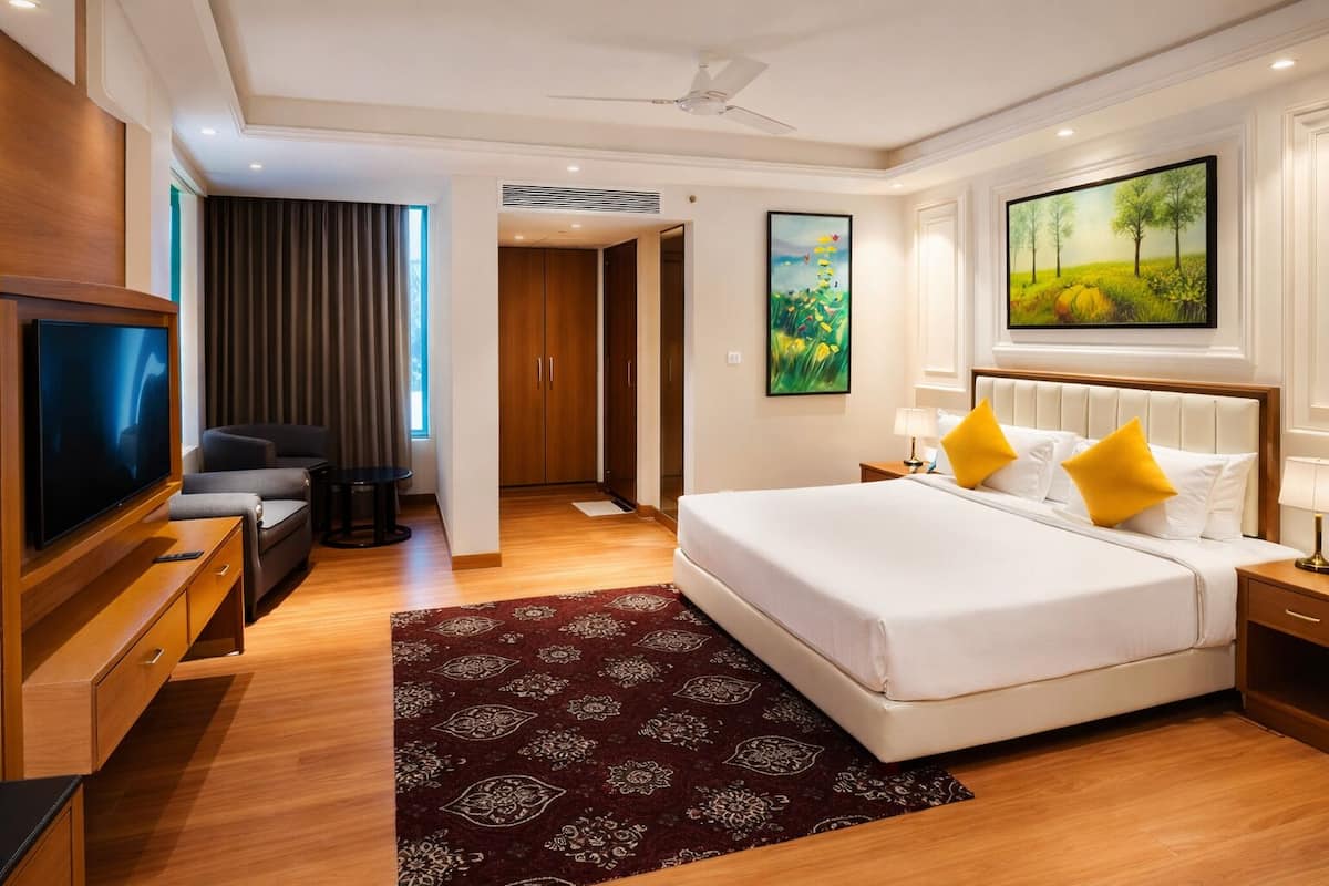 Habitación de hotel con una cama grande, televisión, zona de estar y obras de arte en las paredes.