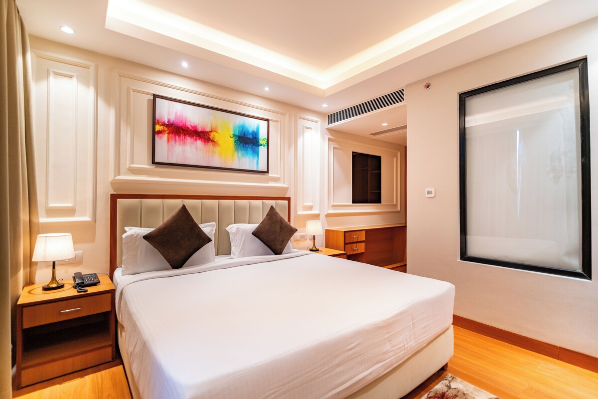 A hotel room with a large bed, bedside tables, a flat-screen TV, and a painting on the wall.