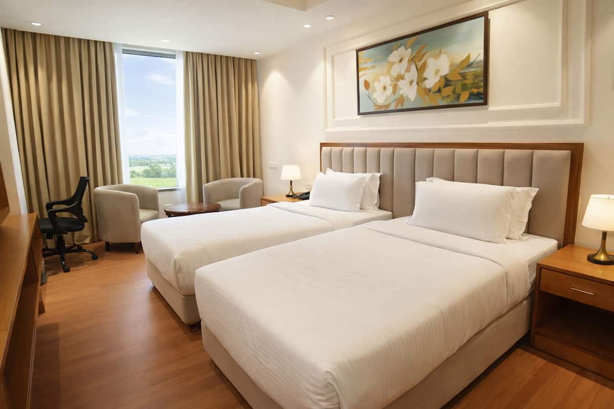 Una habitación de hotel con dos camas, un escritorio, una silla y un cuadro en la pared.